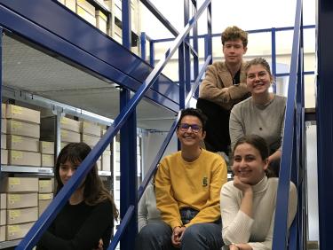Studierende im Depot der GDKE Speyer: Vier Studierende sitzen auf einer blauen Treppe und lächeln in die Kamera.